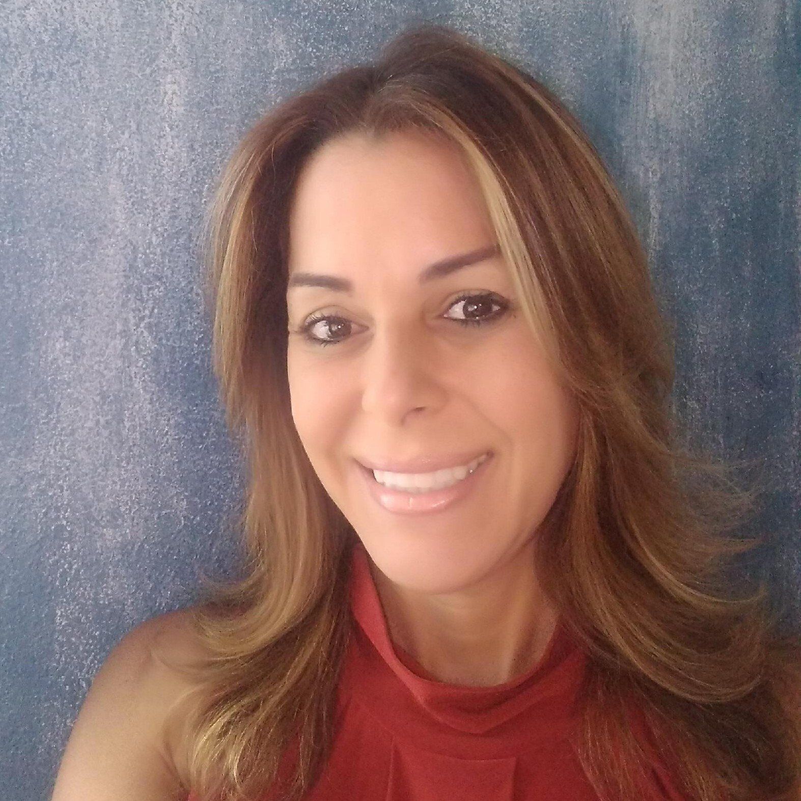 Woman with shoulder-length brown hair and a red shirt smiling in front of a blue wall.