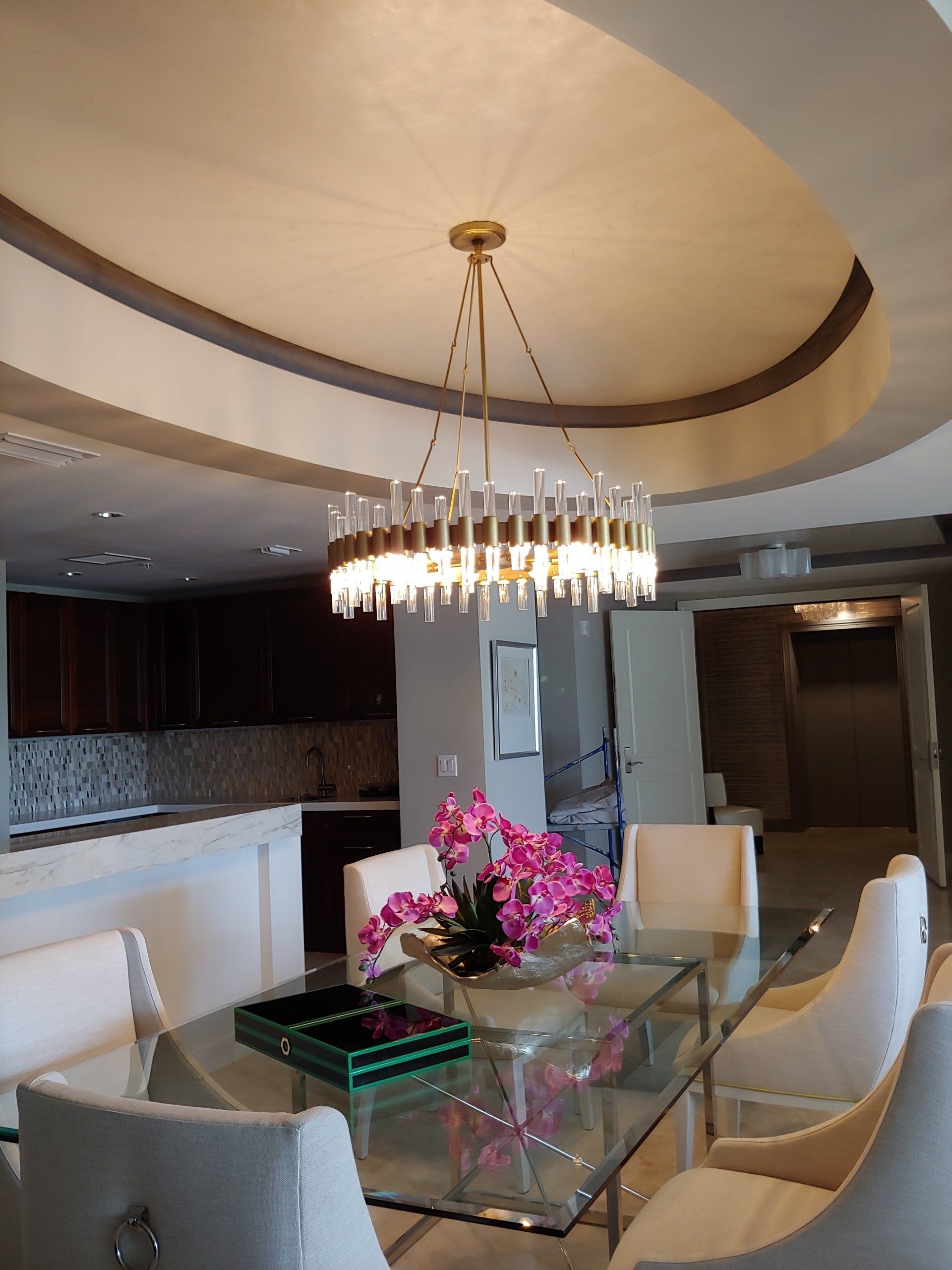 Dining room with glass table, white chairs, and a gold chandelier.