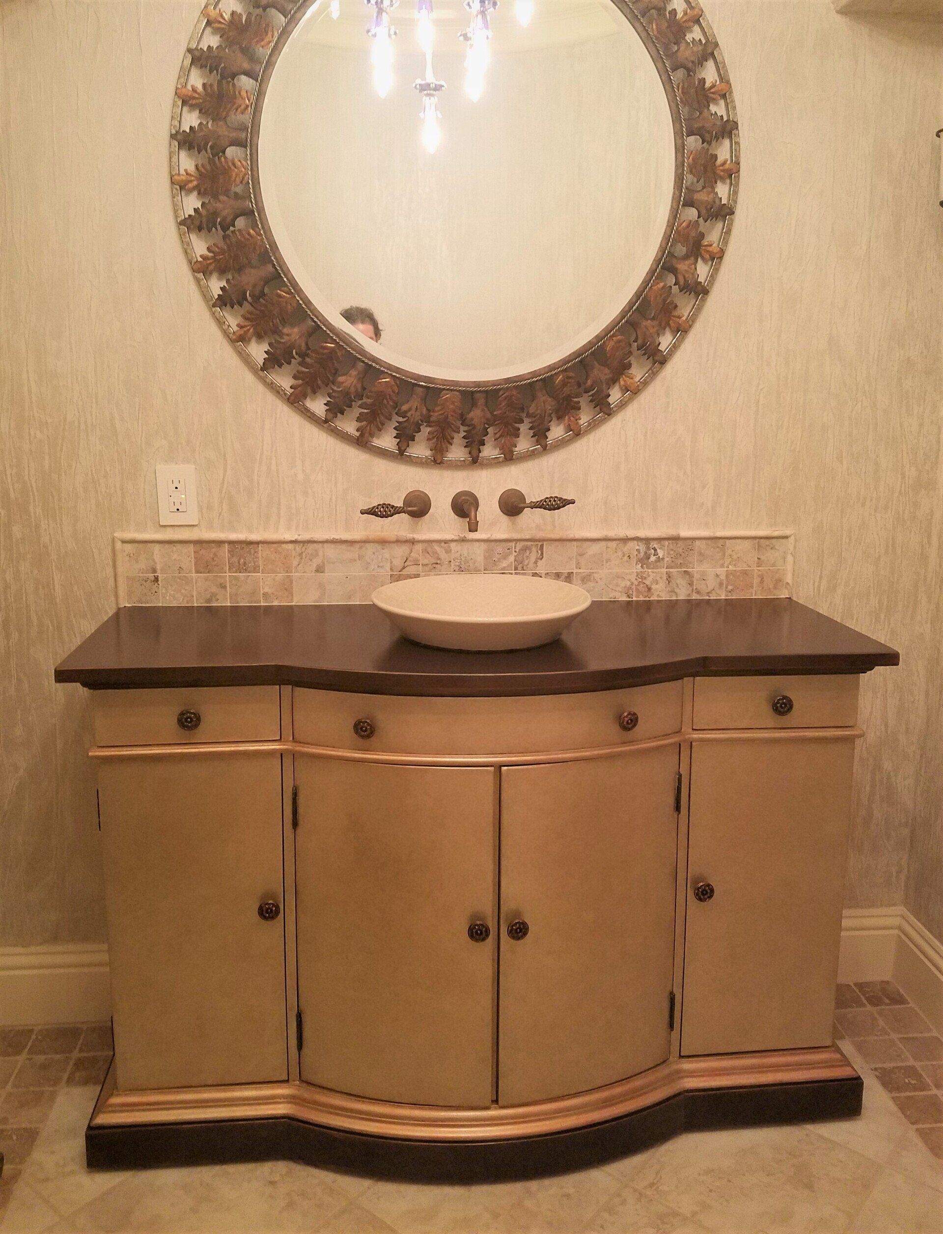 Beige vanity with a dark countertop, round mirror, and vessel sink in a bathroom.