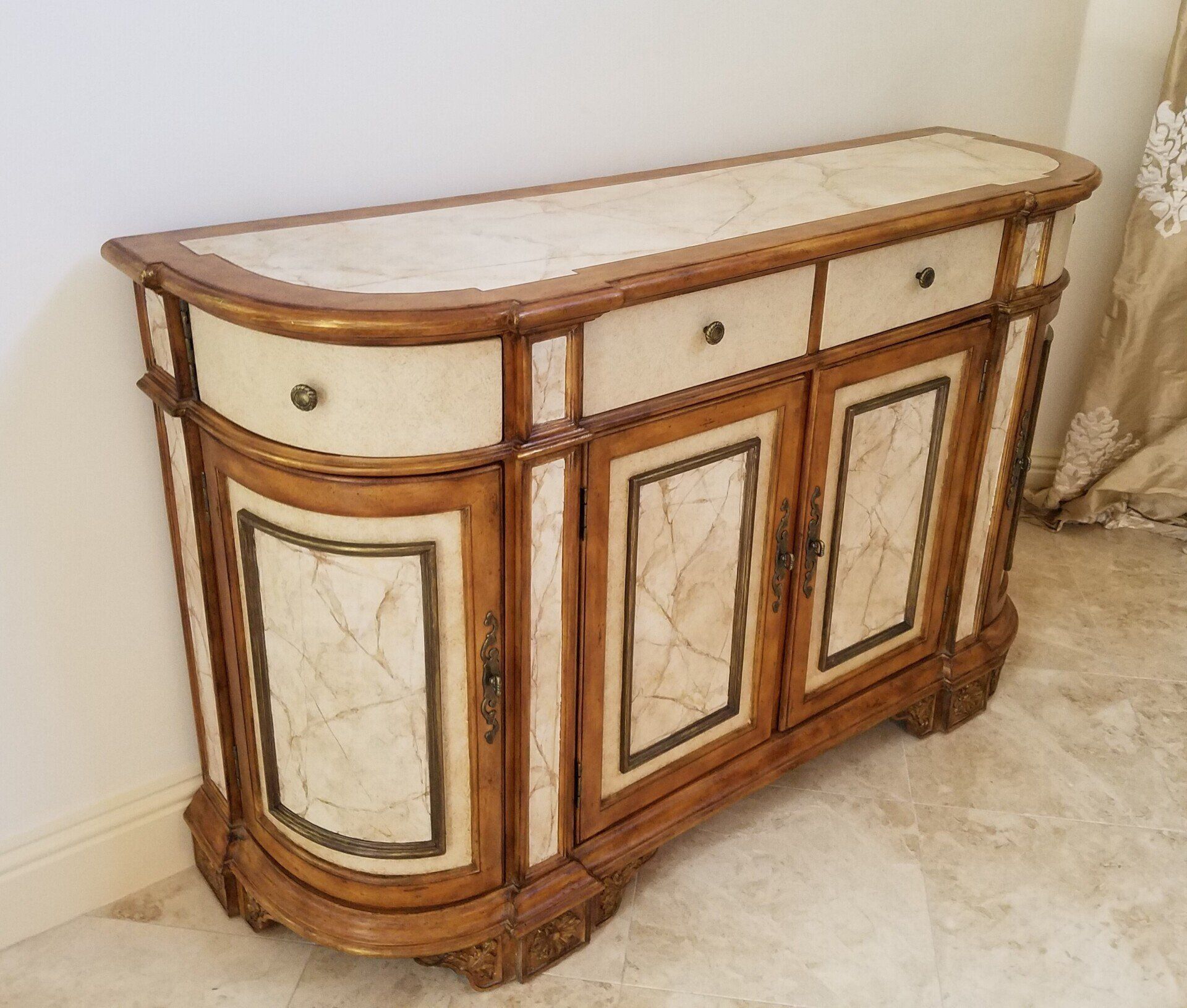 A wooden cabinet with cream and gold detailing and a marble top, against a wall.