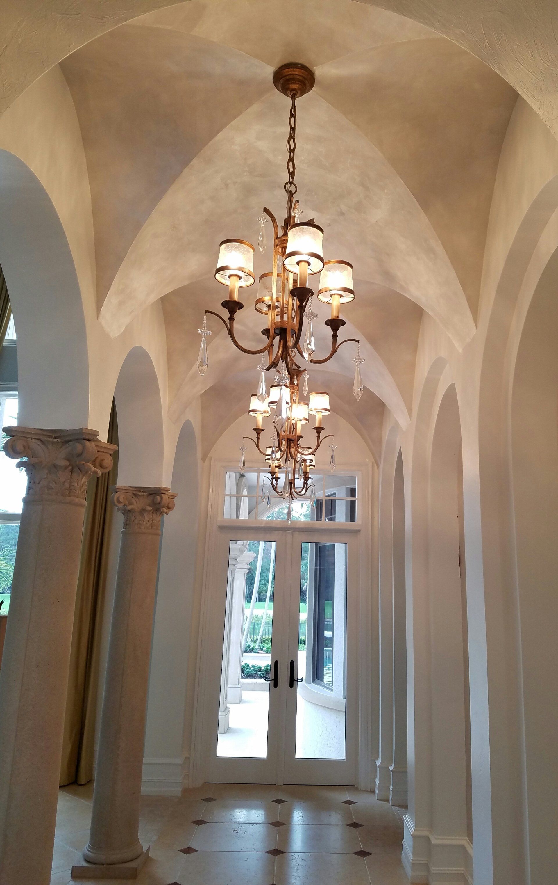 Ornate hallway with arched ceiling, columns, and chandelier leading to French doors.