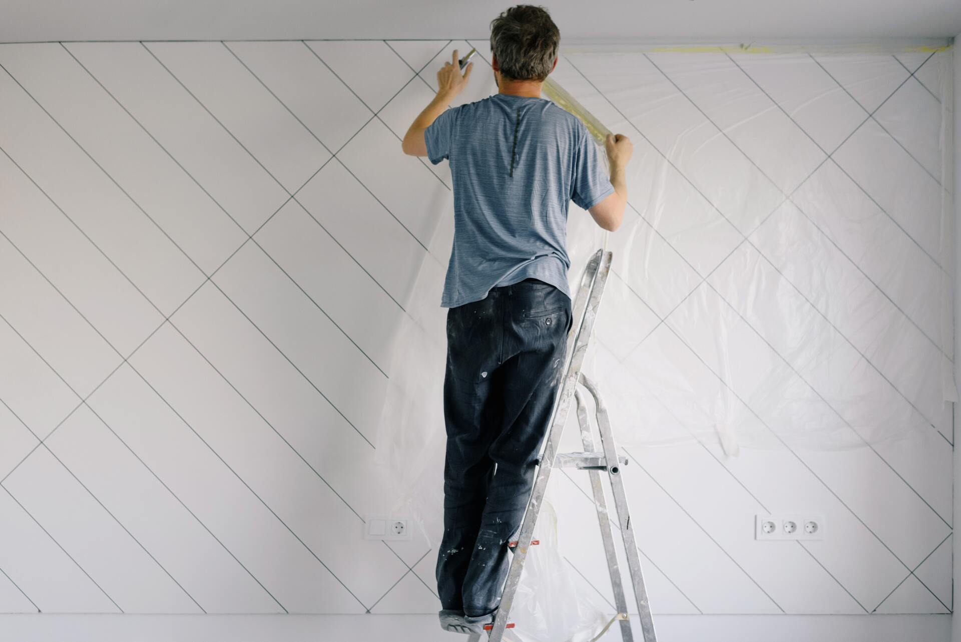 a man standing on a ladder painting a wall.