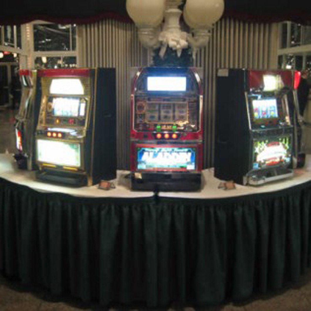 Three slot machines are on a table with a green skirt