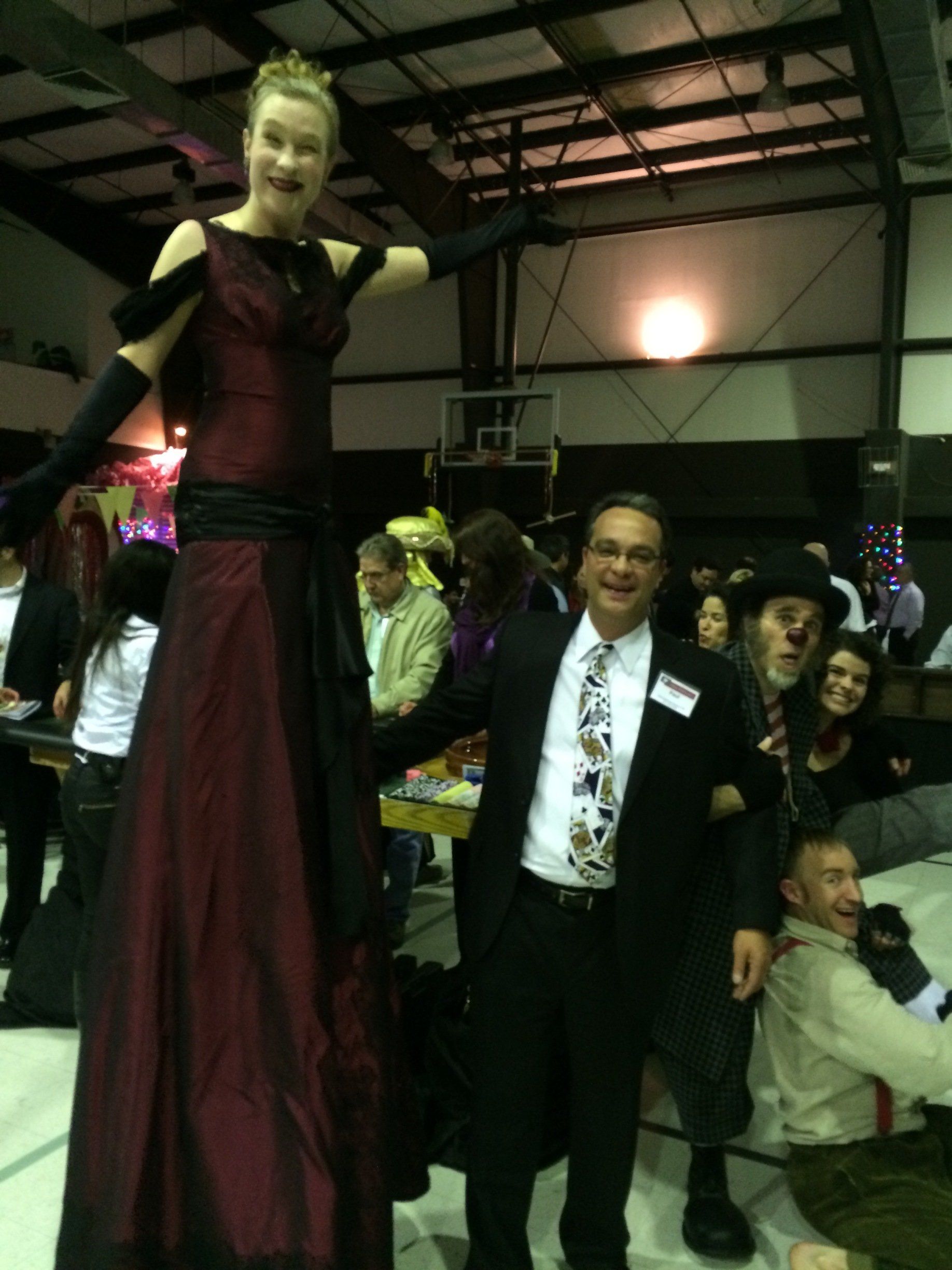 A man in a suit stands next to a woman on stilts