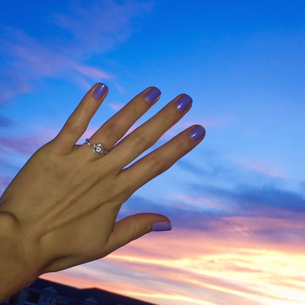 A woman 's hand with purple nails and a ring on her finger