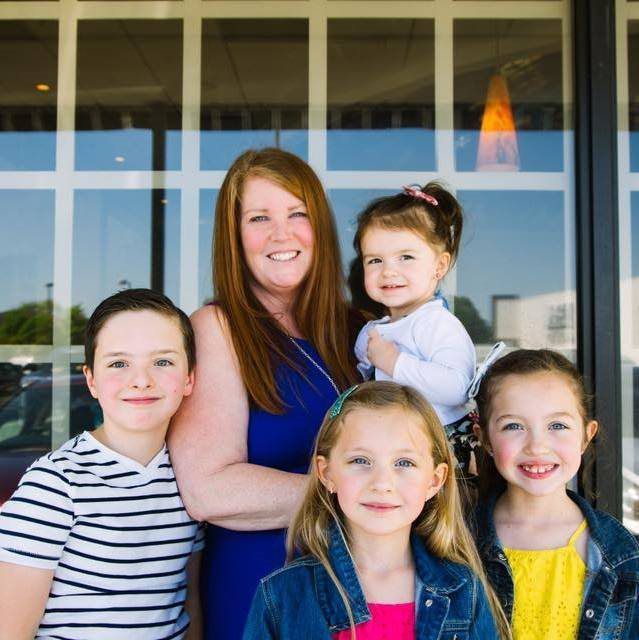 A woman and three children are posing for a picture in front of a window.