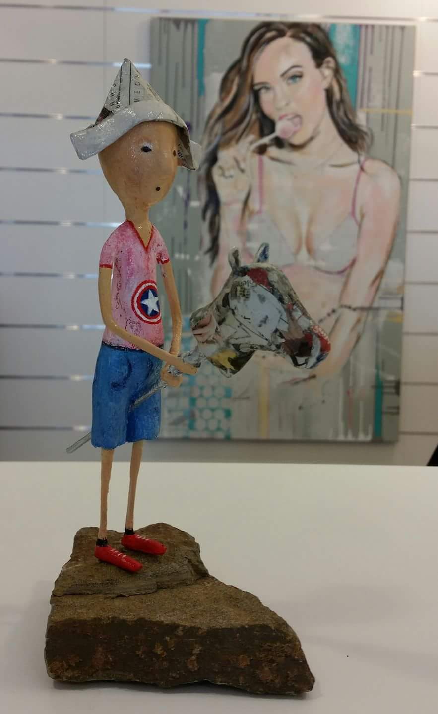 Een standbeeld van een jongen die op een rots staat voor een schilderij van een vrouw.