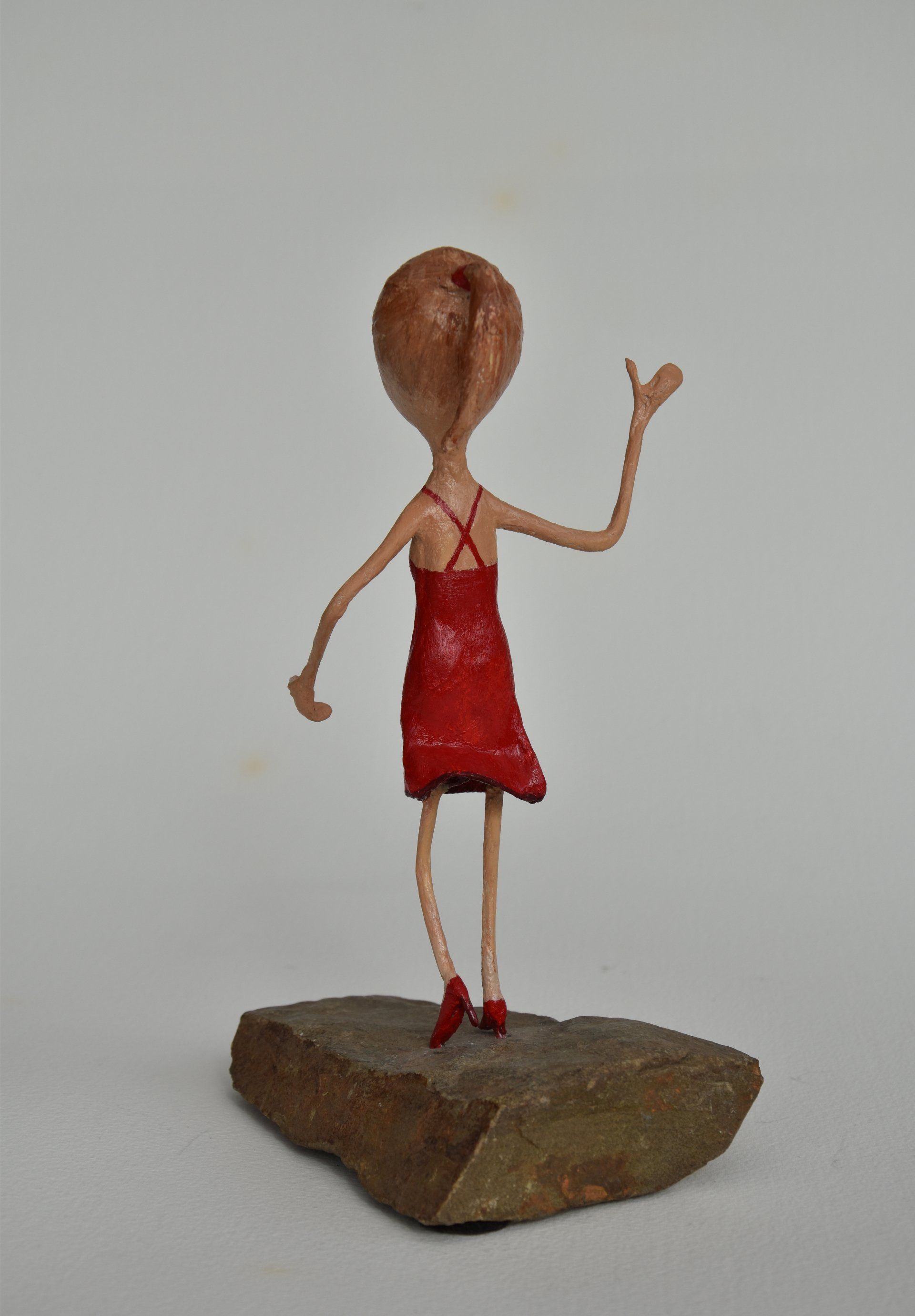 Op een rots staat een standbeeld van een vrouw in een rode jurk.