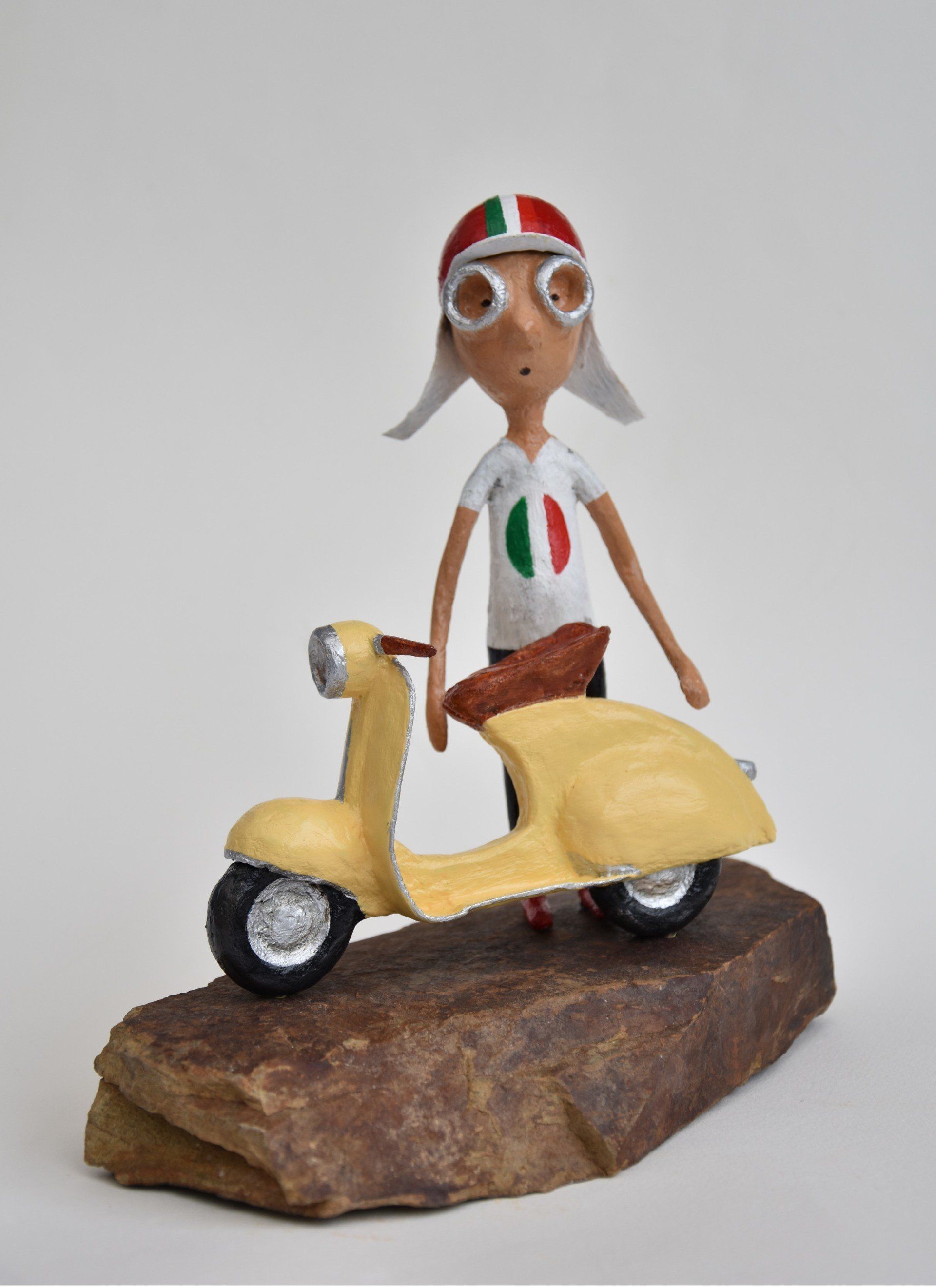 Een beeldje van een jongen die op een gele scooter rijdt