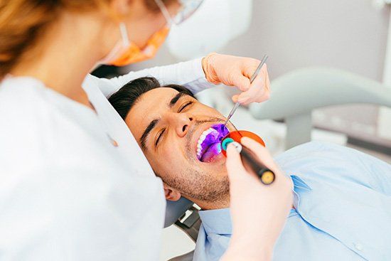 Dentist using a curing light on a patient's tooth in a dental office. The patient has his eyes closed.
