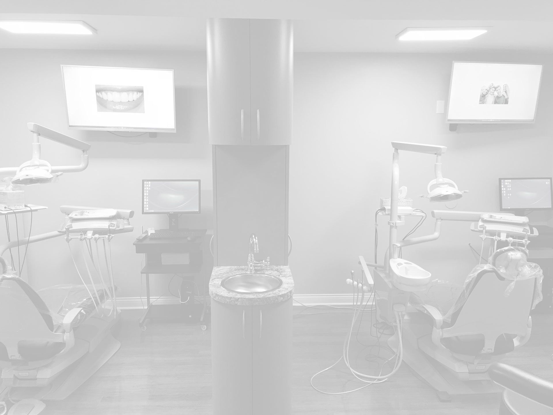 Two dental chairs and equipment in a bright, modern dentist's office. Two screens are visible.