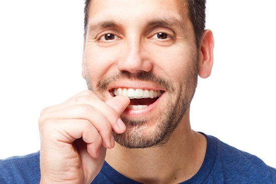 Man smiling, picking teeth with a fingernail. He's wearing a blue shirt, set against a white background.