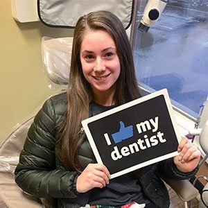 Woman at dentist's office smiling, holding a sign that says