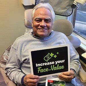 Man in dentist chair smiles, holding sign: 