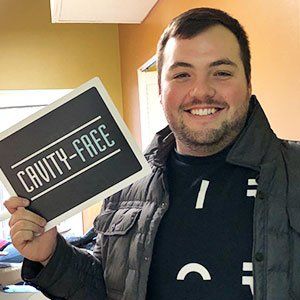 Man smiling, holding a sign that reads 