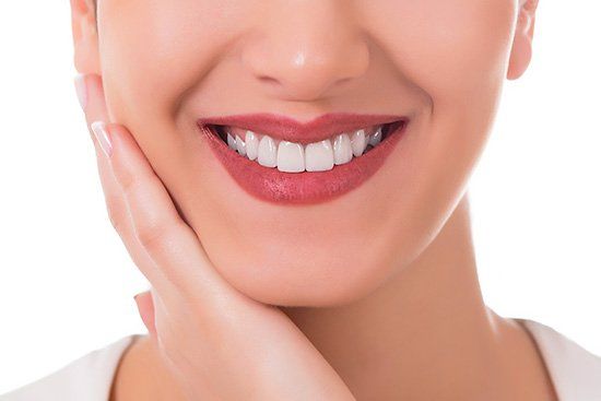 Close-up of a woman smiling, showing perfect white teeth and a hand touching her cheek.