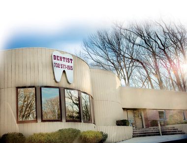 Exterior of a dentist's office with a large tooth sign, tan building, and trees.