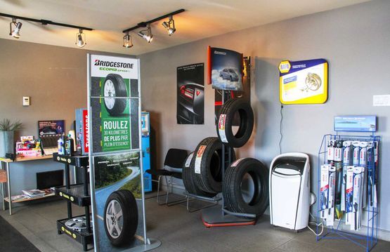 Salle d'exposition d'un magasin de pneus avec des pneus empilés, des présentoirs de jantes et des produits d'entretien automobile sur des étagères.