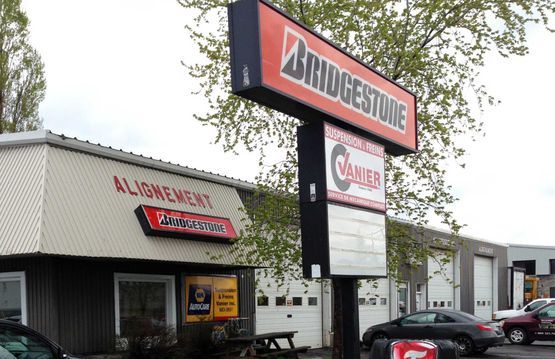 Façade d'un magasin de pneus Bridgestone et Firestone avec une grande enseigne en bord de route et des voitures garées