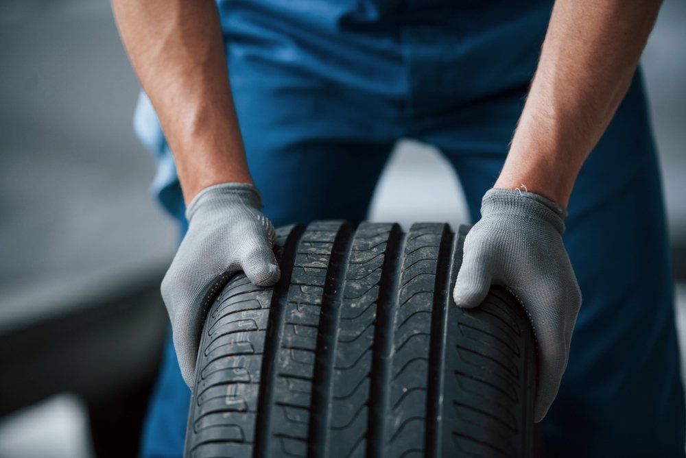 Des mains gantées tiennent un pneu de voiture à sculptures profondes dans un garage