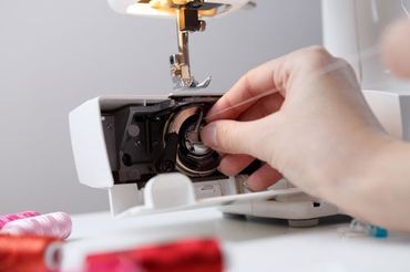 una mano che inserisce un filo dentro a una macchina da cucire