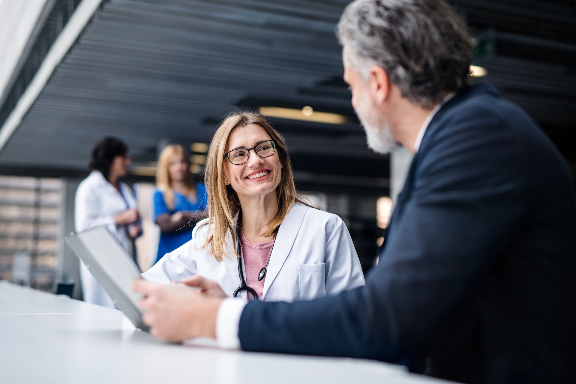 A woman doctor is sitting at a table talking to a man in a suit.