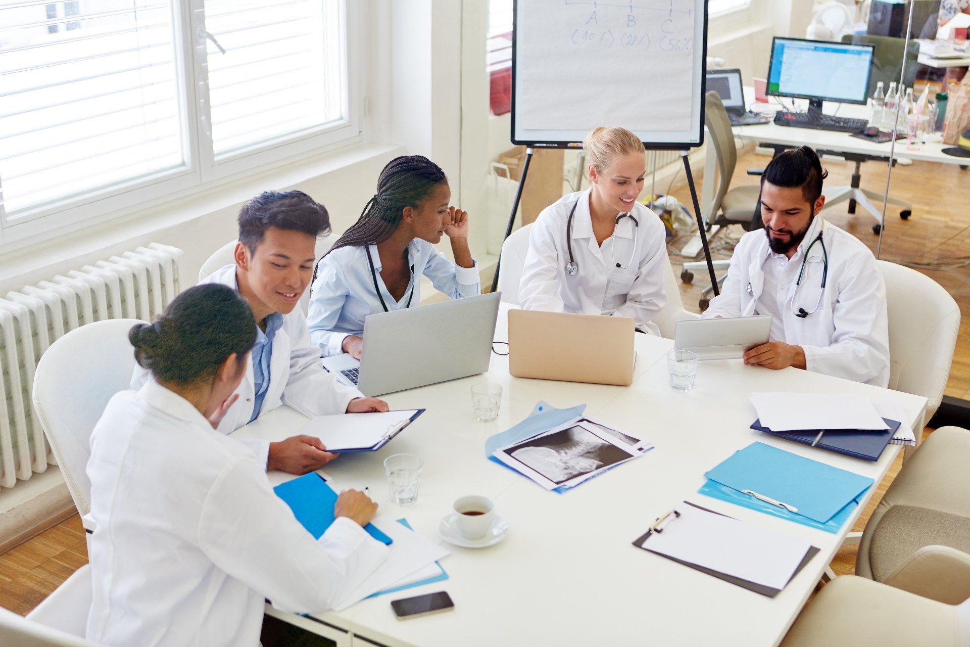 A group of doctors are sitting around a table with laptops.
