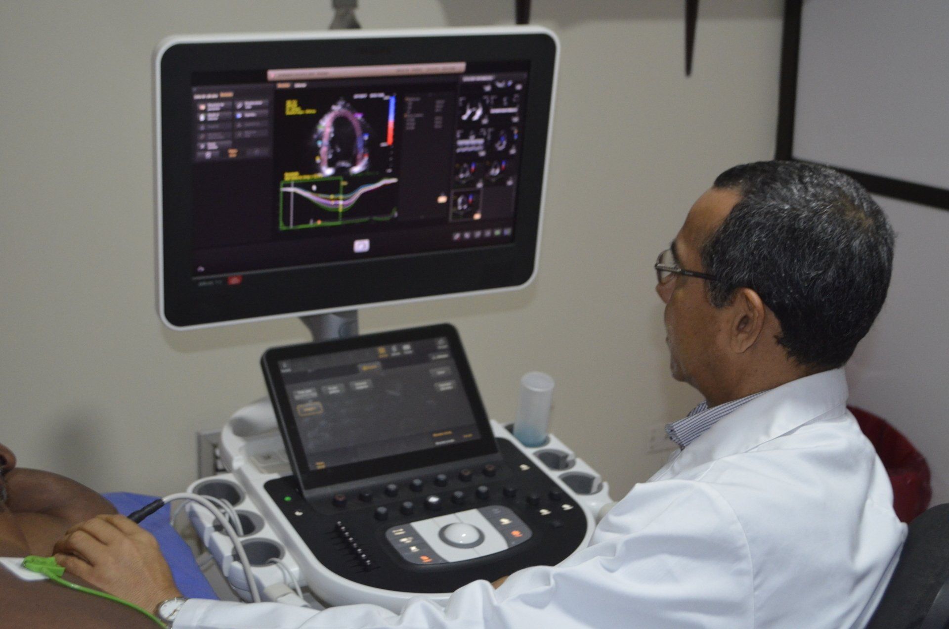 A medical professional performs a diagnostic ultrasound, viewing images on a screen while seated next to a patient.