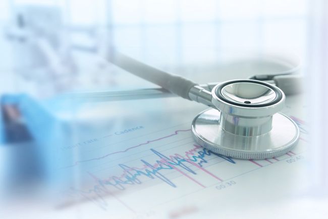 A silver stethoscope resting on a printed medical chart with EKG wave patterns, set against a blurred, bright background.