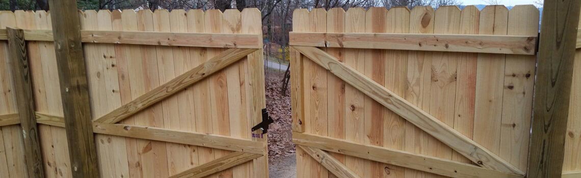 Wooden fence with open gates, a tree trunk in the center, and a rural setting.