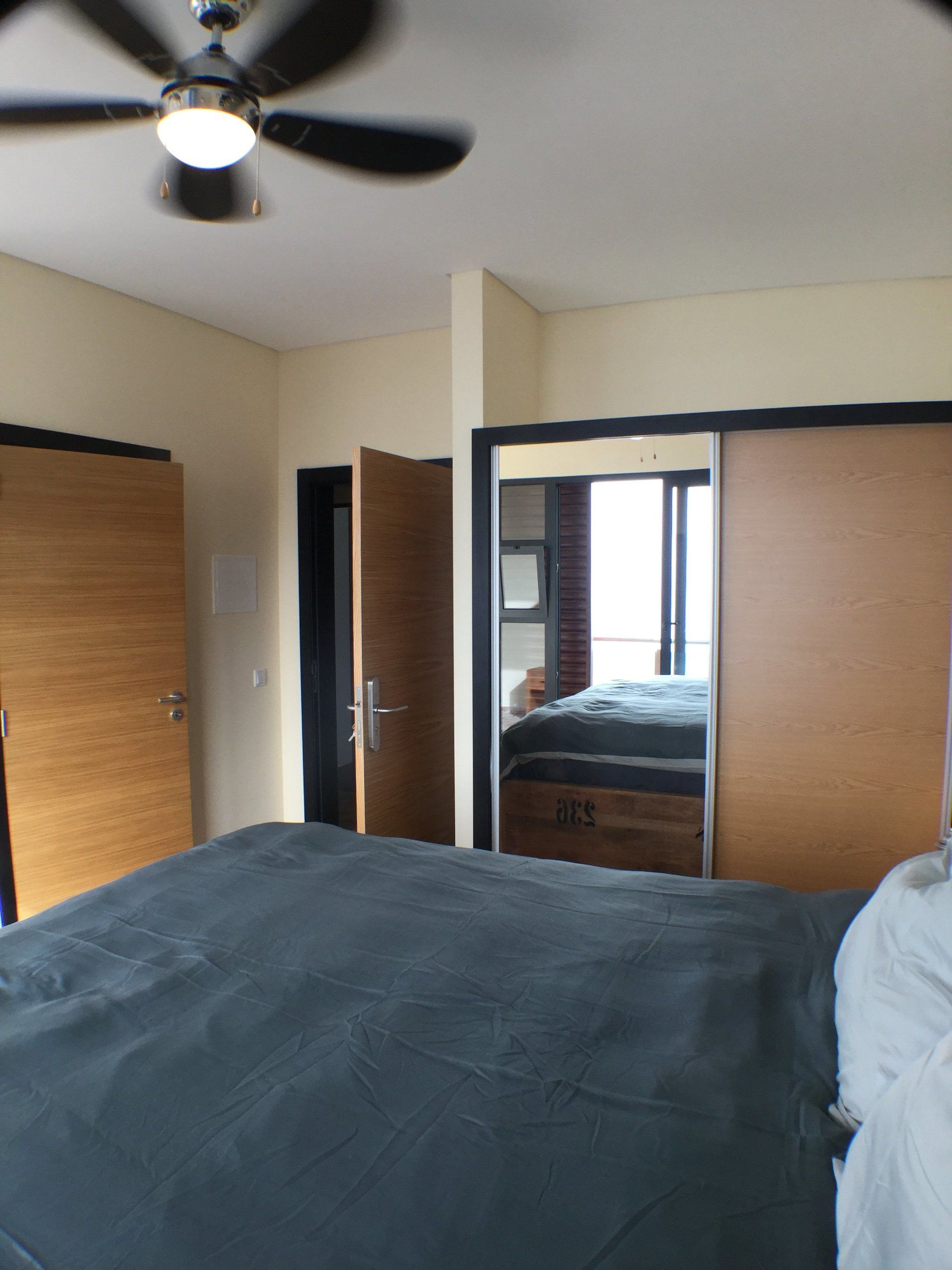 Schlafzimmerinterieur mit Bett, Schiebetüren zum Kleiderschrank, Deckenventilator und offener Tür zu einem anderen Zimmer.