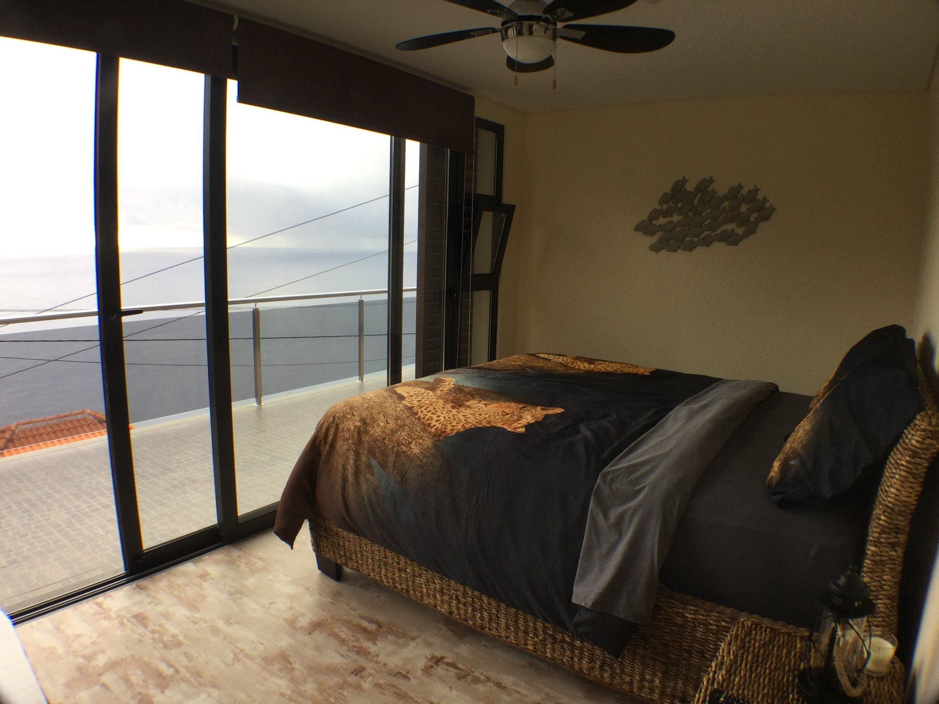 Schlafzimmer mit Bett, großem Fenster mit Meerblick, brauner Bettwäsche und hellen Wänden.