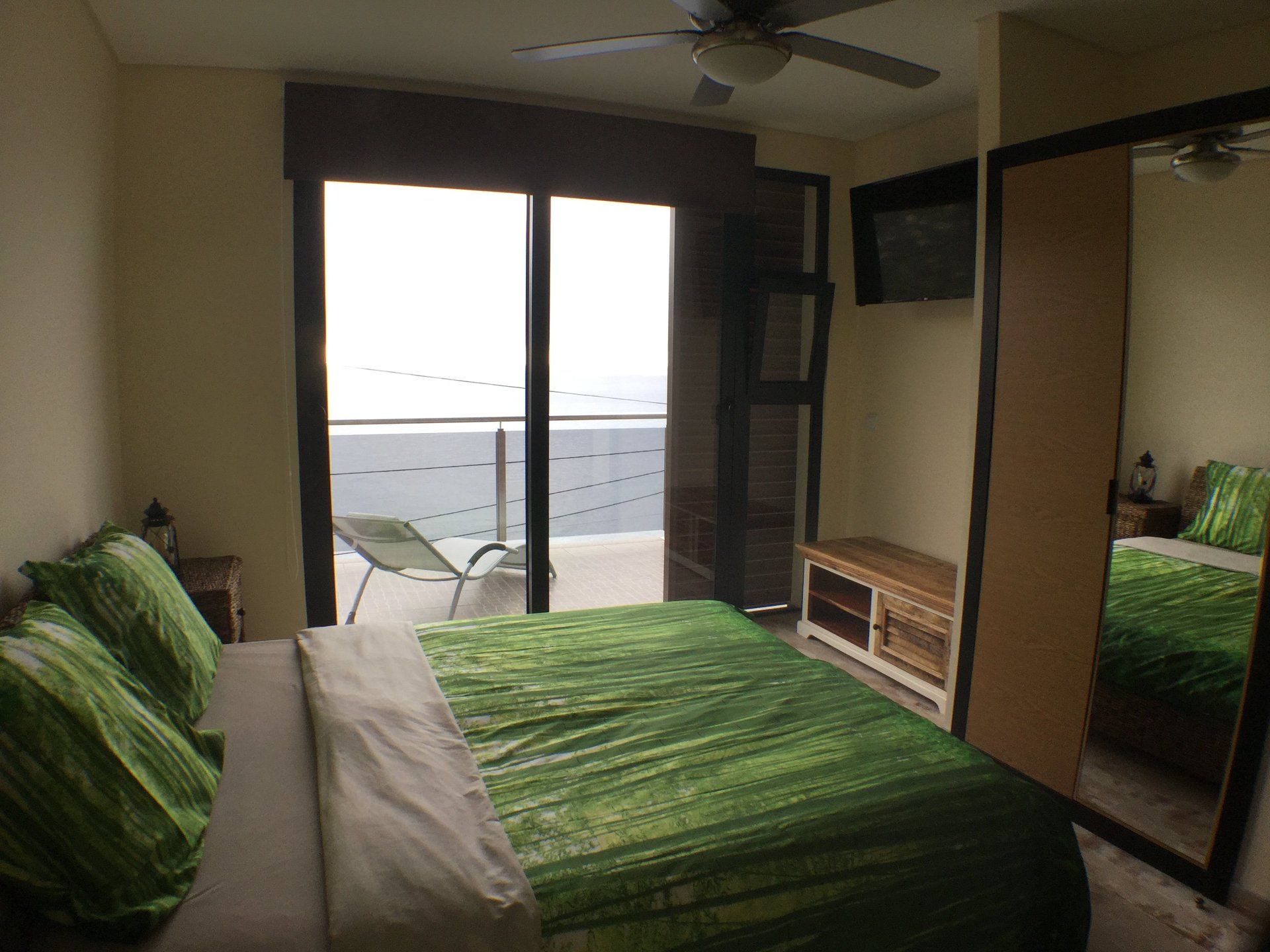 Schlafzimmer mit grüner Tagesdecke, Balkon mit Meerblick und einem großen Spiegel.