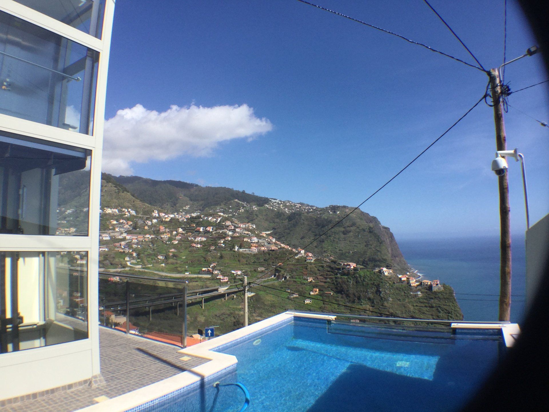 Pool mit Blick auf das Meer und ein Hügeldorf unter blauem Himmel.