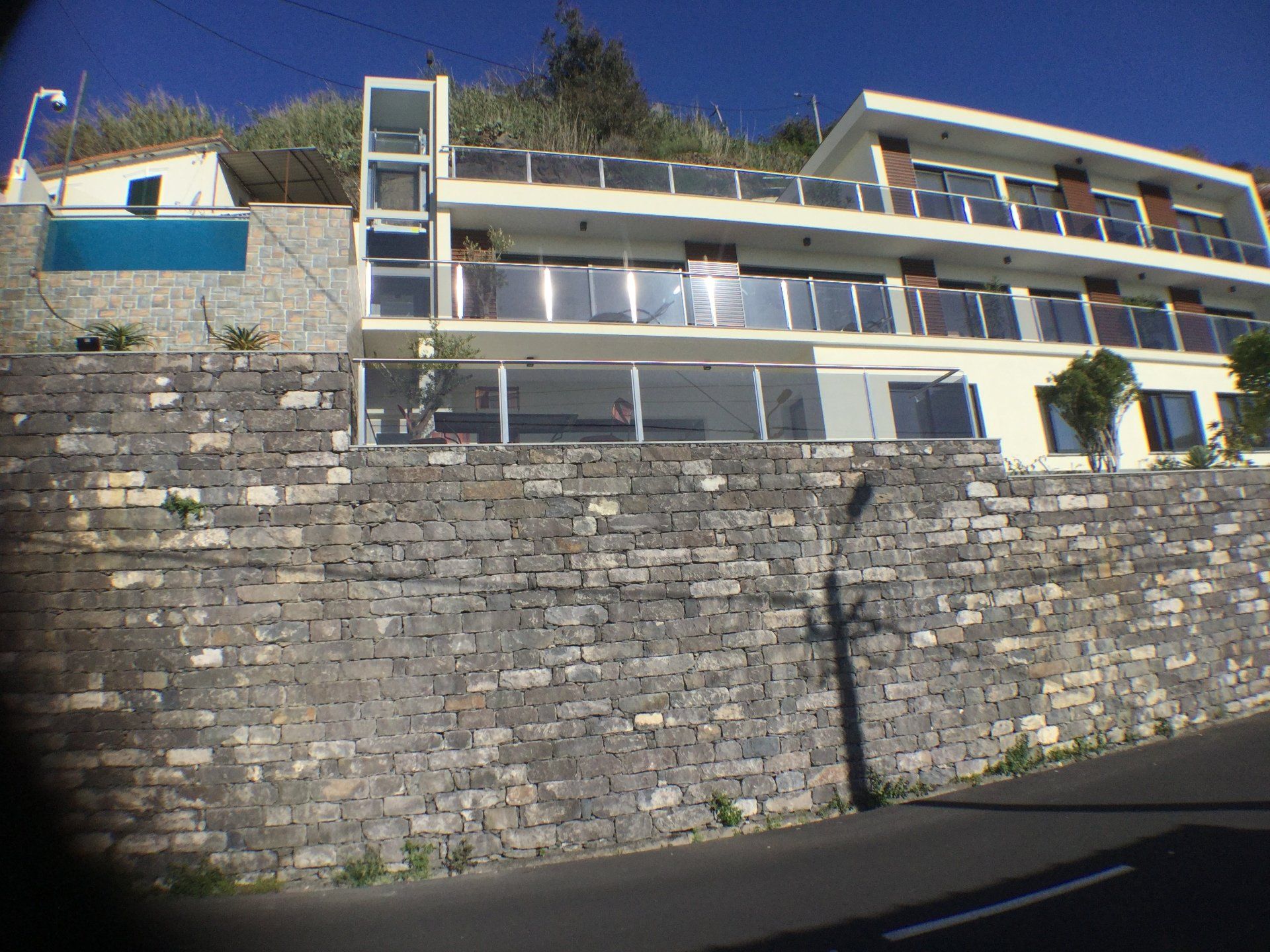 Modernes Gebäude mit Glasbalkonen, in einen Hang gebaut, auf einer steinernen Stützmauer.