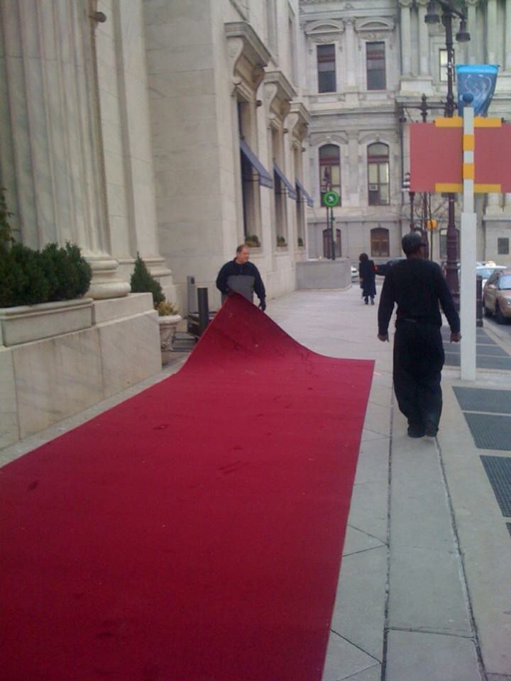 A red carpet is being rolled out on the sidewalk