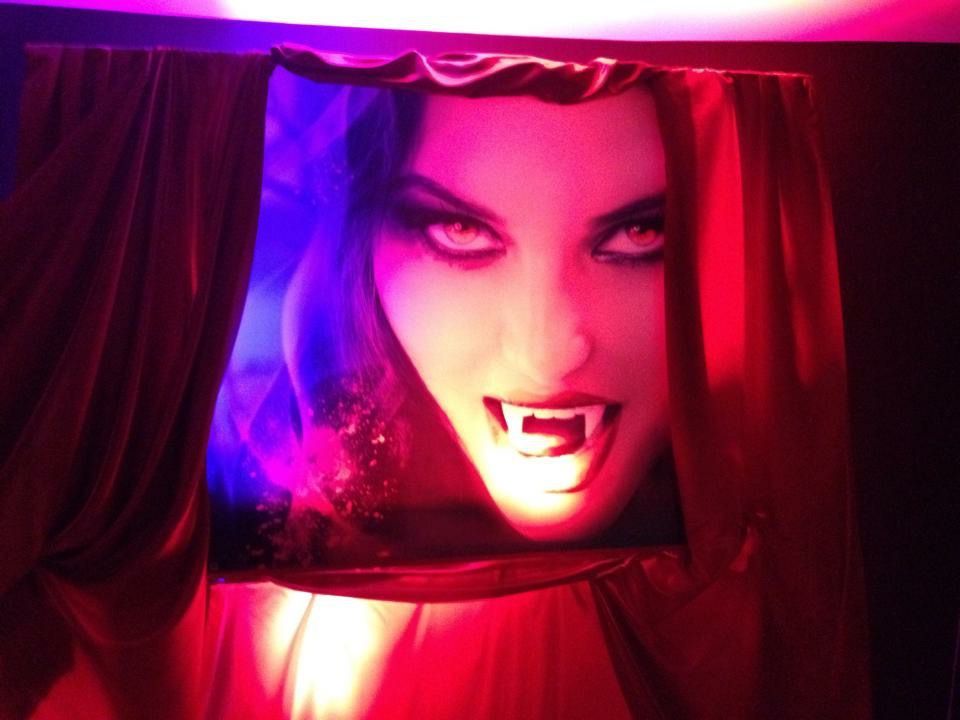 A picture of a woman with vampire teeth behind a red curtain