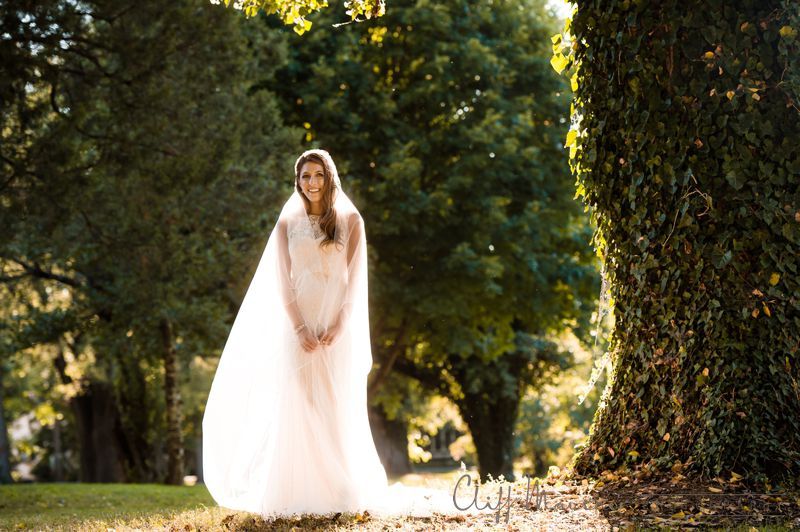 A woman in a wedding dress and veil is standing in a park.