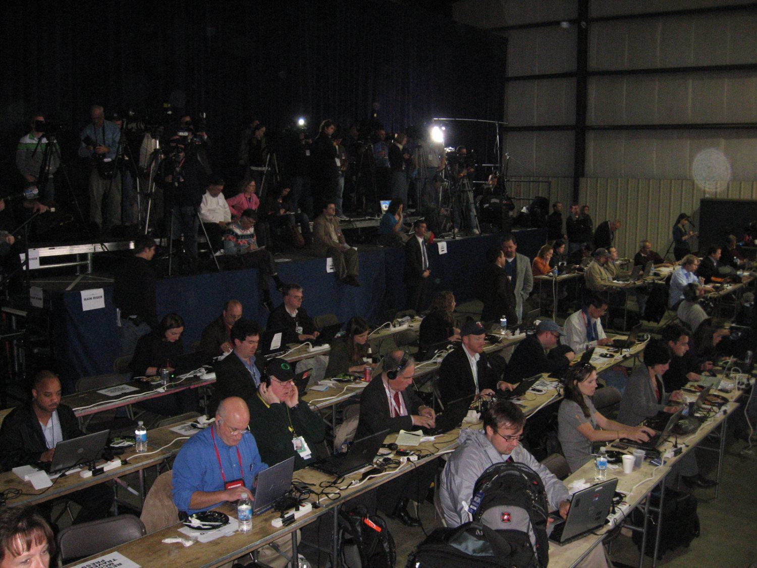 A large group of people are sitting at tables with laptops