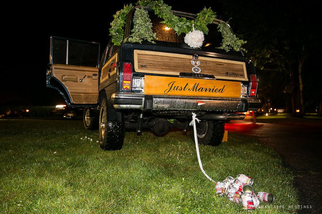 A black suv with a just married sign on the back is parked in the grass.