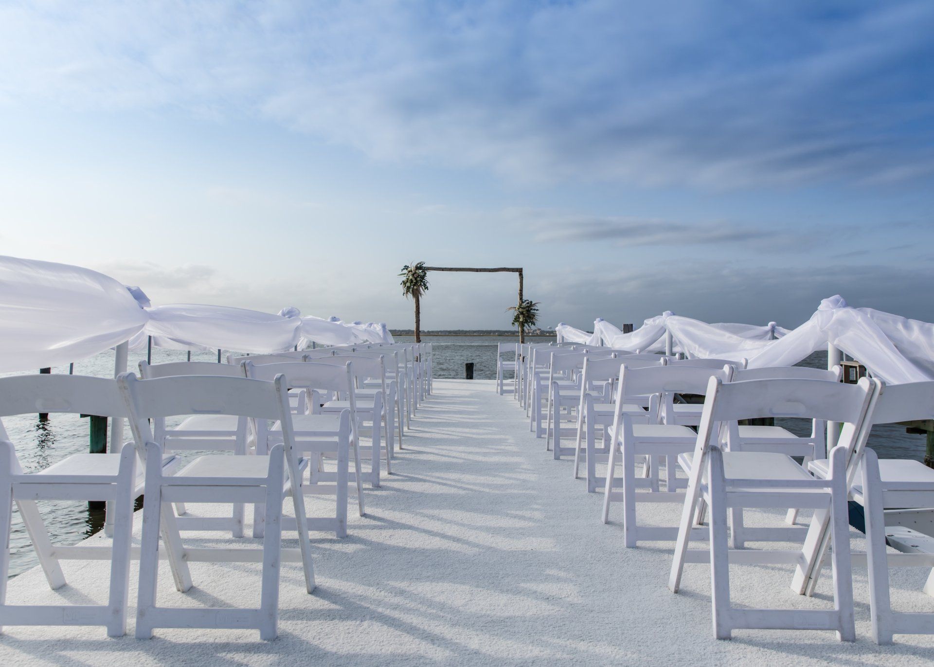 A row of white folding chairs are lined up on a dock.