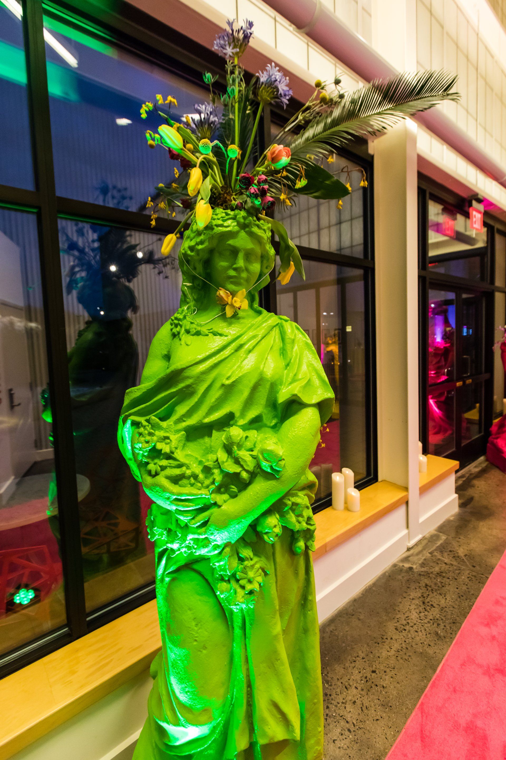 A green statue of a woman with flowers on her head.