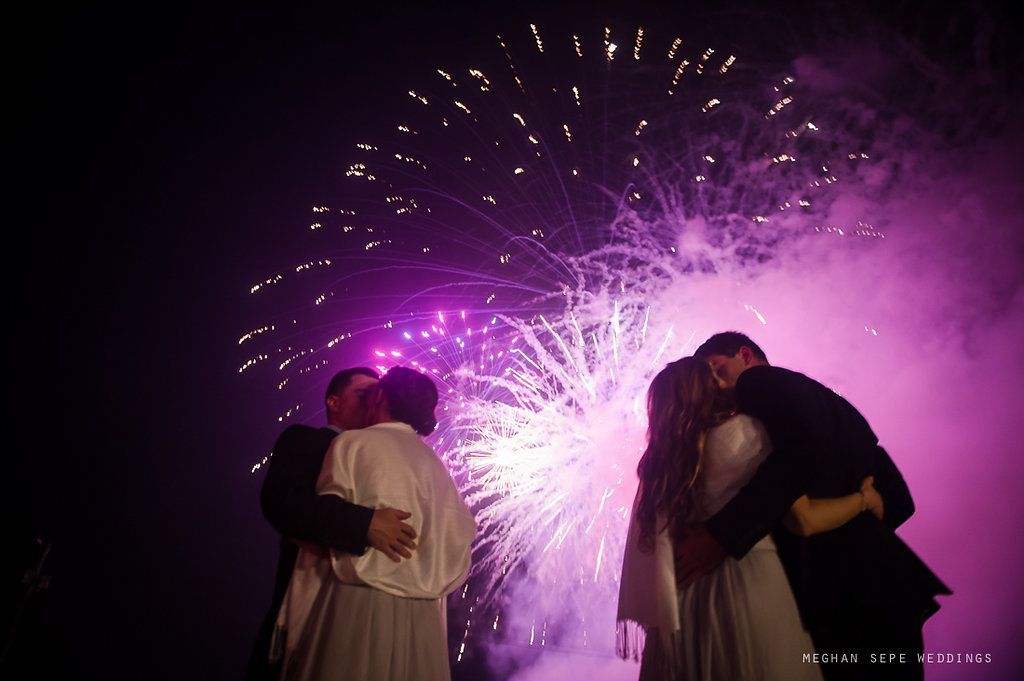 A bride and groom kissing in front of a fireworks display.