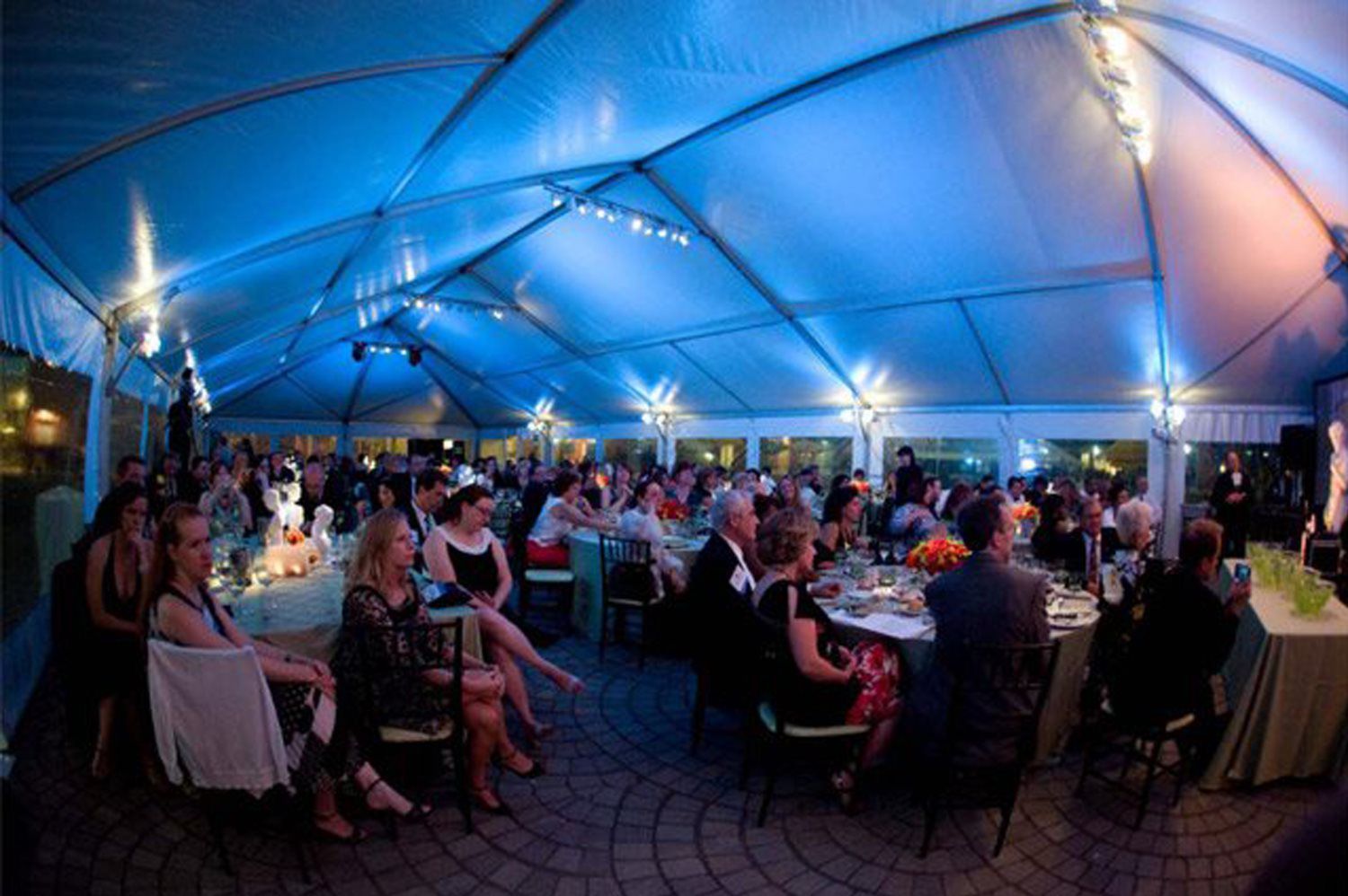 A large group of people are sitting at tables under a tent.