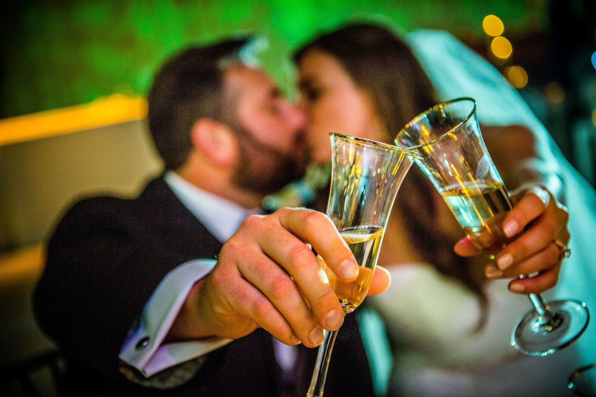 A bride and groom are kissing while toasting with champagne glasses.