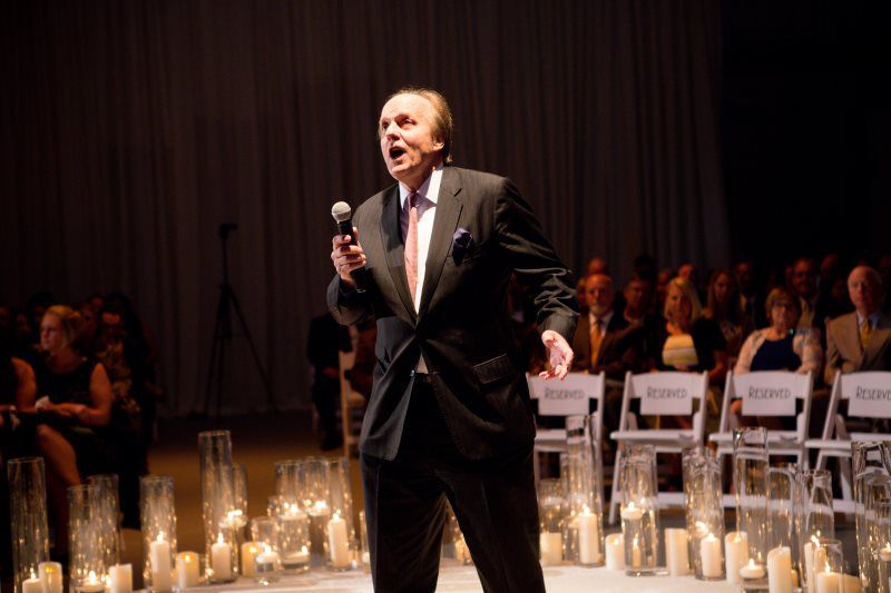 A man in a suit is holding a microphone in front of a crowd of people
