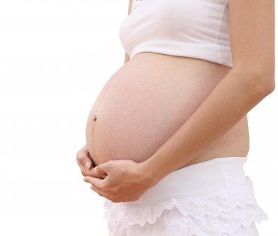 A pregnant woman in a white top and white skirt is holding her pregnant belly