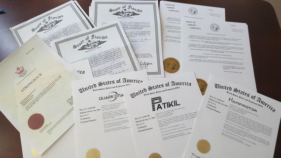 Pile of official documents with seals and ornate borders, some from the US, on a brown surface.