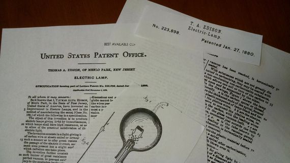 Patent documents and a handwritten note on a desk. Focus on a lightbulb patent.