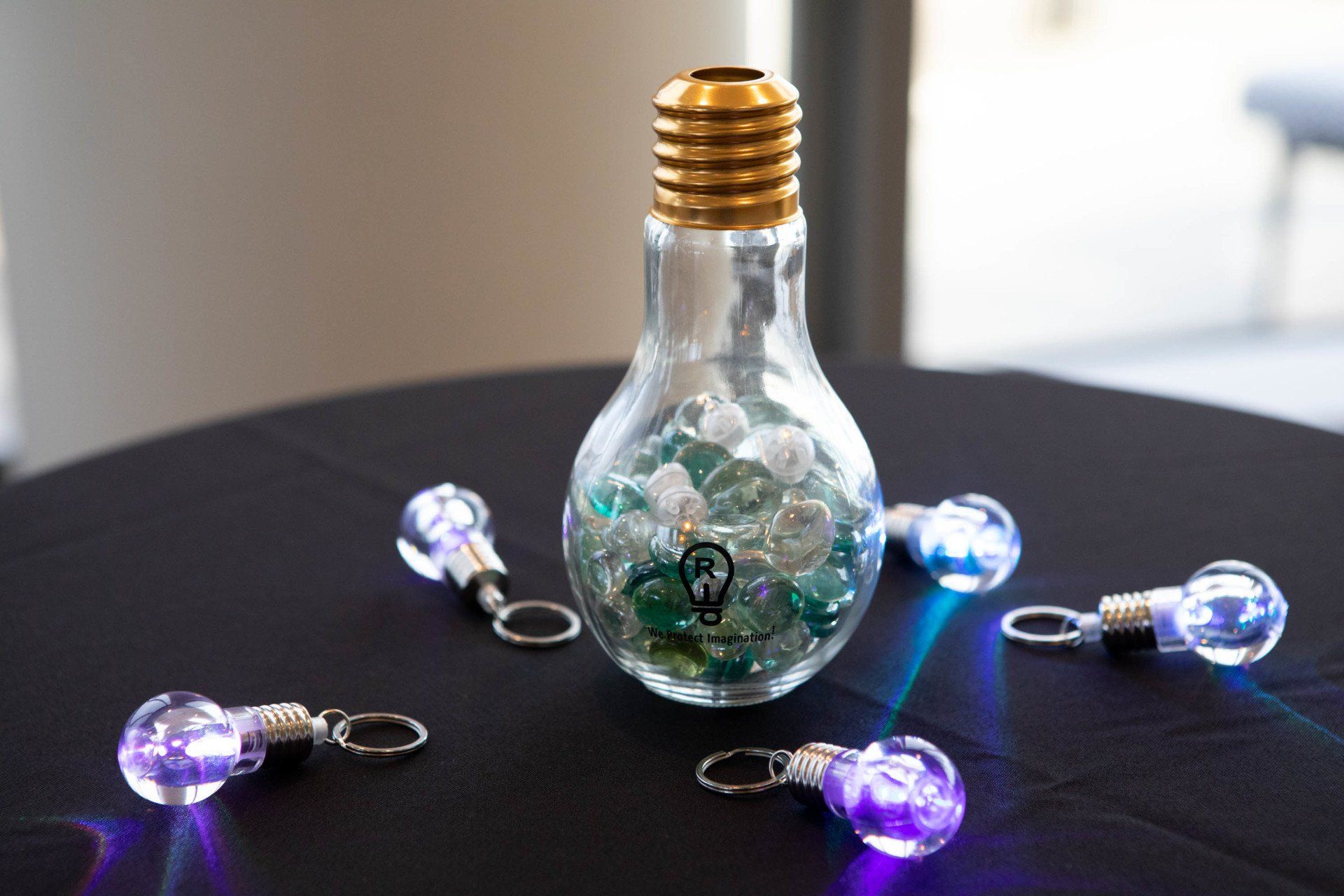 Lightbulb-shaped glass container and keychains with glowing lights on a black table.